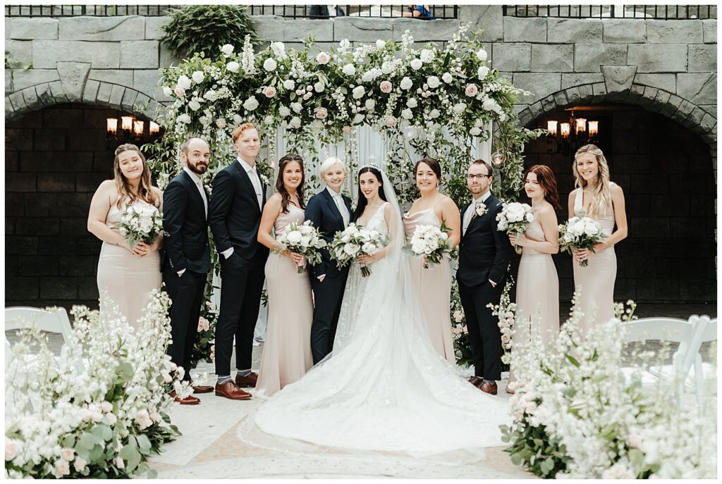 portrait of wedding party standing at floral altar at garden-themed wedding