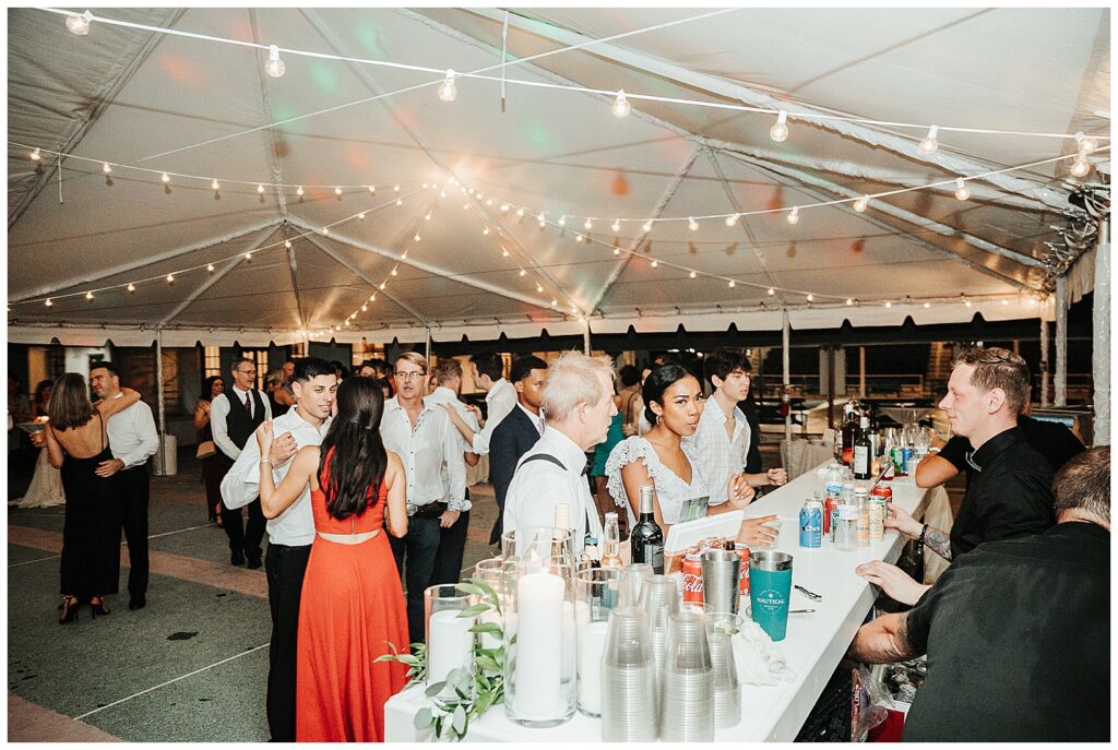 Wedding guests dance next to bar in romantically lit outdoor tent