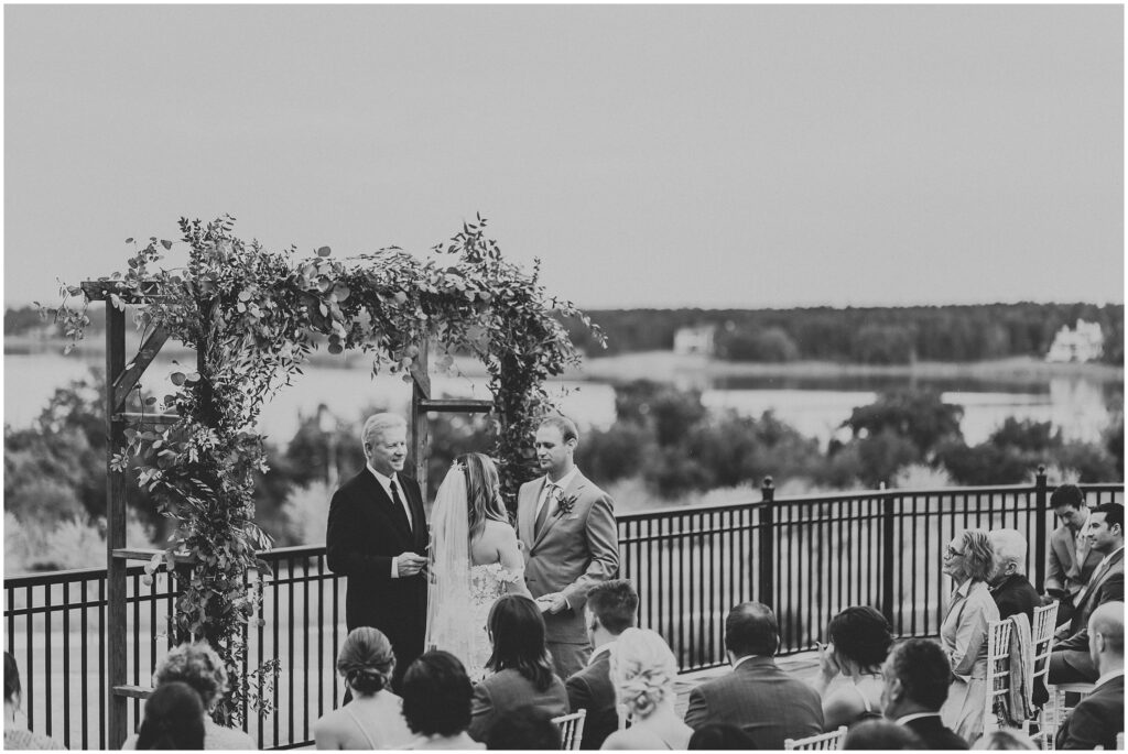 Romantic black-and-white outdoor lakefront wedding photo of bride and groom at altar