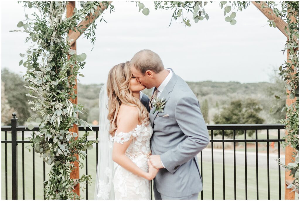 blonde woman in white dress holding hands with man in suit and sharing first kiss as husband and wife; Florida outdoor wedding first kiss portrait