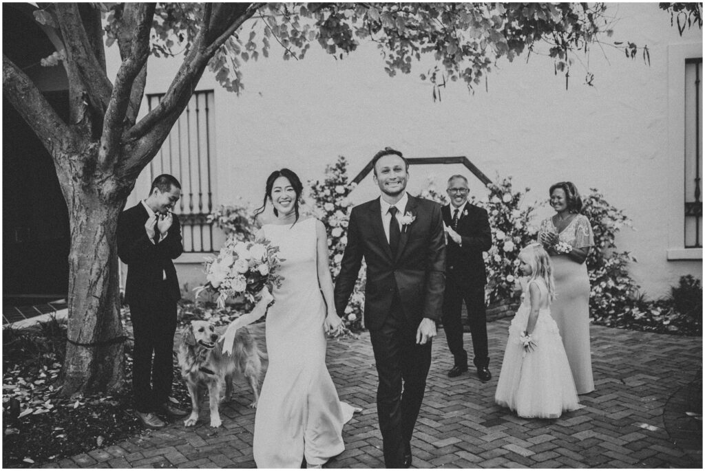 black and white photo of smiling bride and groom walking side-by-side holding hands after wedding ceremony at St. Pete Museum of Fine Arts