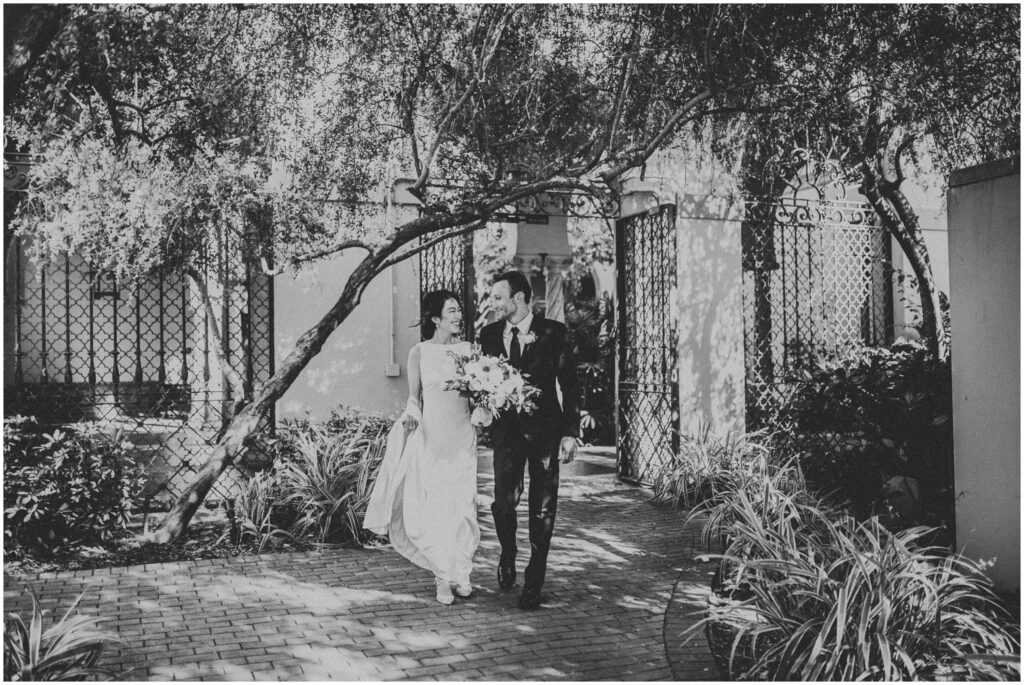 black-and-white photo of bride and groom walking down courtyard of St. Petersburg Museum of Fine Arts on wedding day; garden wedding portrait
