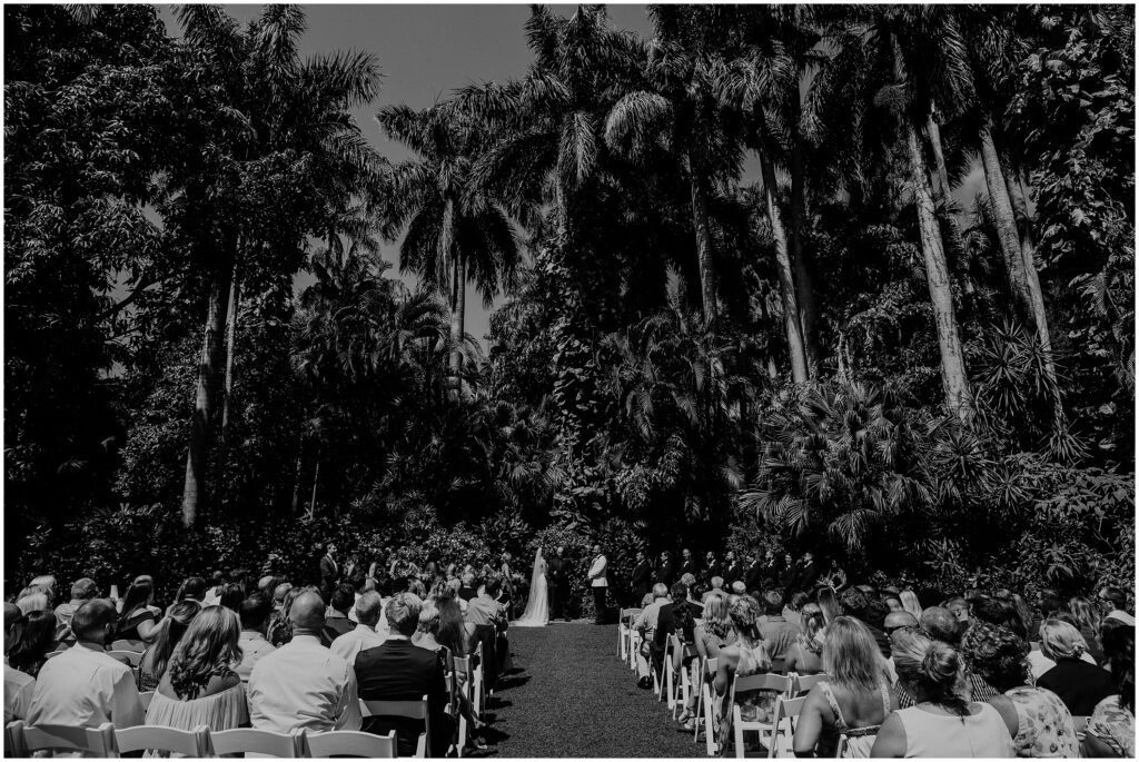 Bride and groom stand at altar surrounded by lush palm trees during Sunken Gardens wedding 