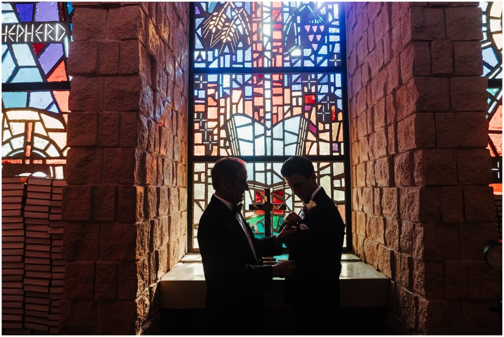 Groom and father's silhouettes in front of stained glass window pane on wedding day