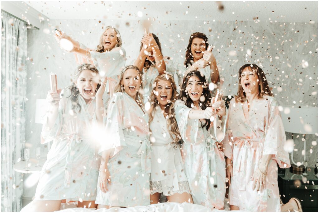 Portrait of bride and bridesmaids wearing silk robes, smiling as confetti falls around them. Bridesmaids getting ready photos 