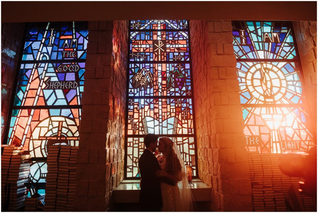 Romantic photo of bride and groom embracing in front of stained glass windows at church during traditional classic wedding