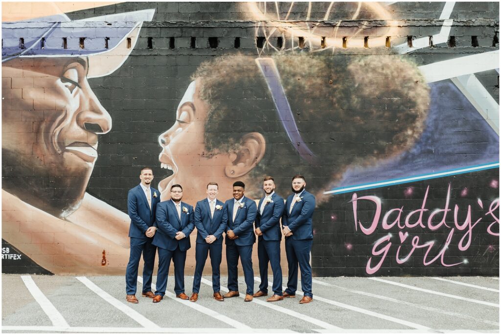 Groomsmen in suits pose in front of Kobe and Gianna Bryant mural in Tampa, Florida before Armature Works wedding 