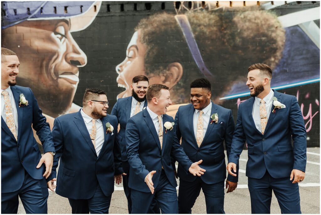 Groomsmen in navy suits with orange ties smile in front of Kobe and Gianna Bryant mural in downtown Tampa 