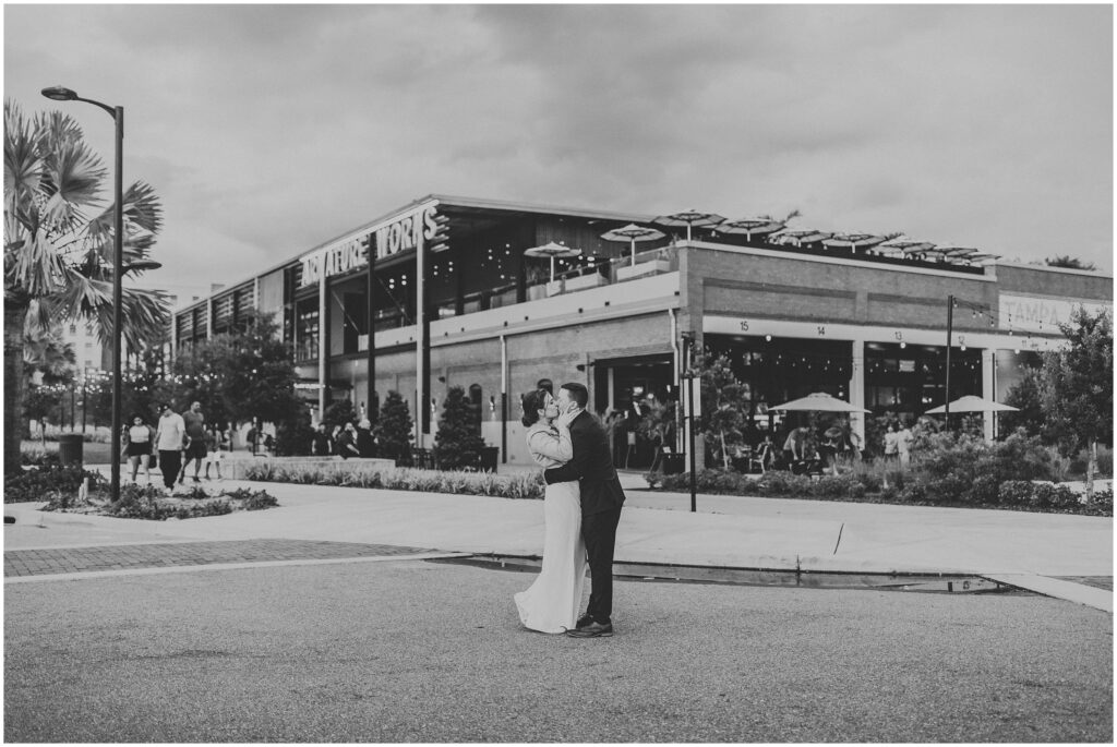 Black and white photo of bride and groom kissing outside in front of Armature Works after wedding