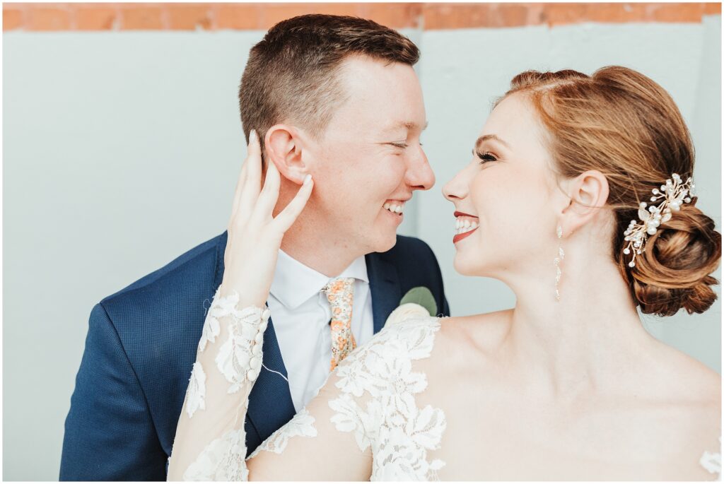 Red-haired bride in lace gown and groom in navy suit look into each other's eyes while they smile 