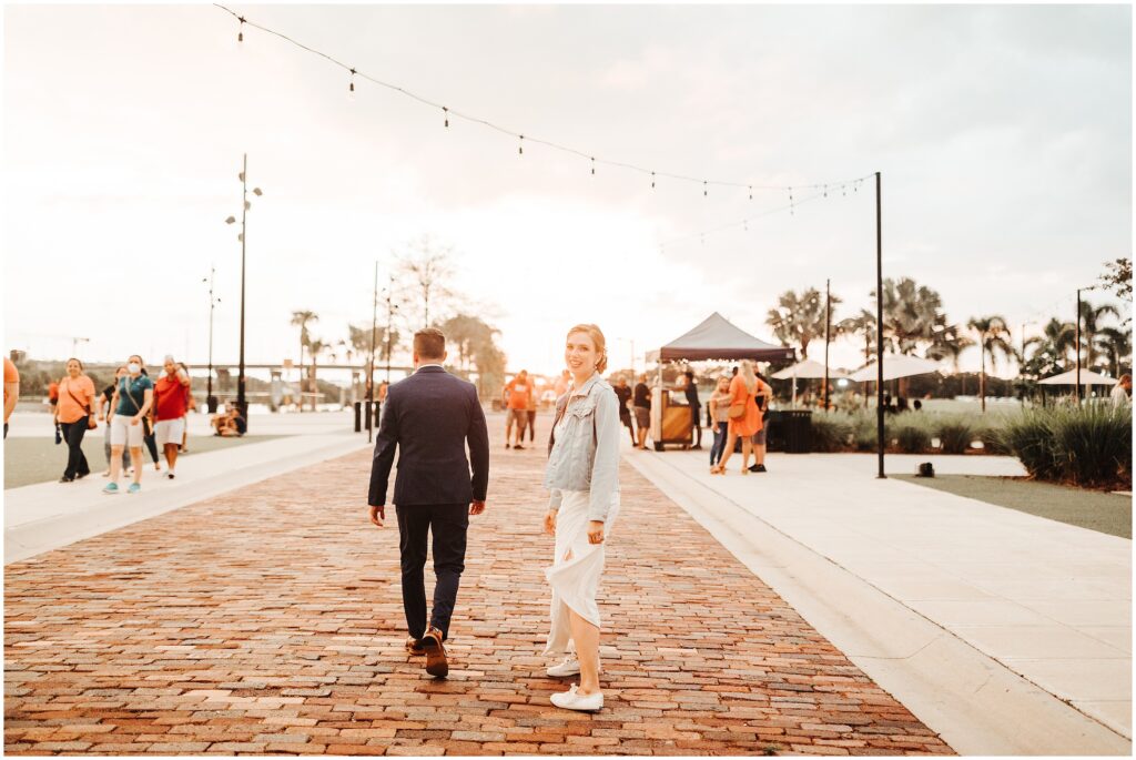 Bride in wedding gown, jean jacket and sneakers smiles and walks with groom outside of Armature Works