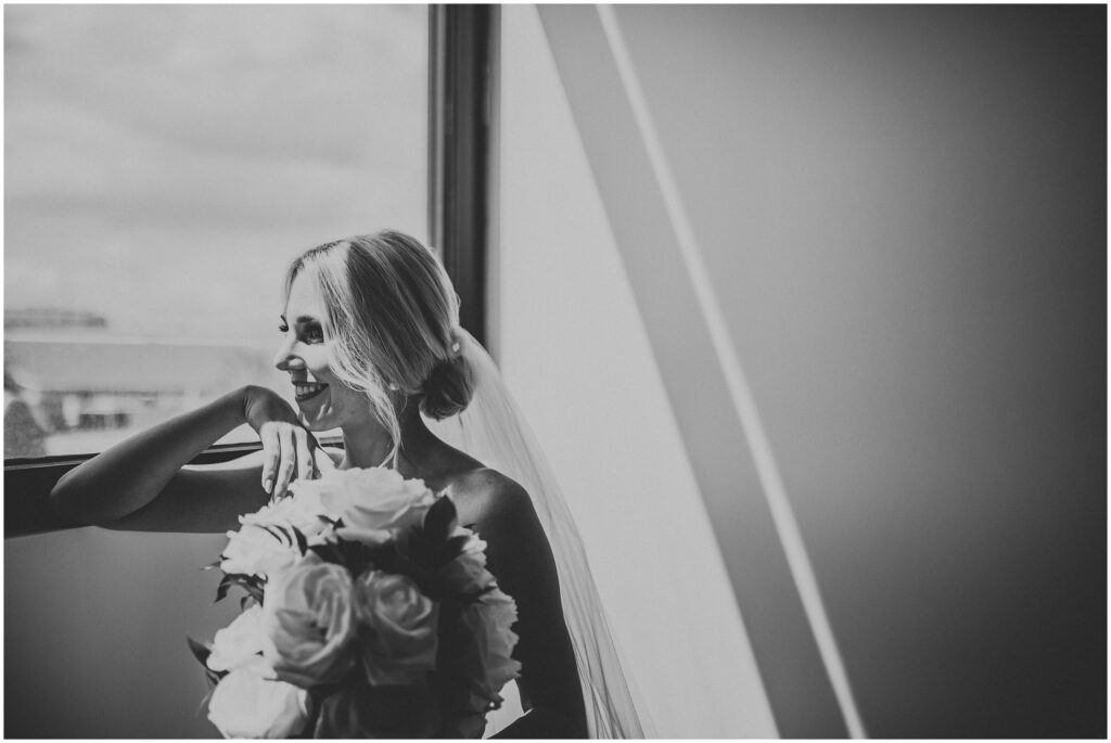 Black and white photo of blonde bride looking out of window and smiling before Hyde House Tampa Wedding 
