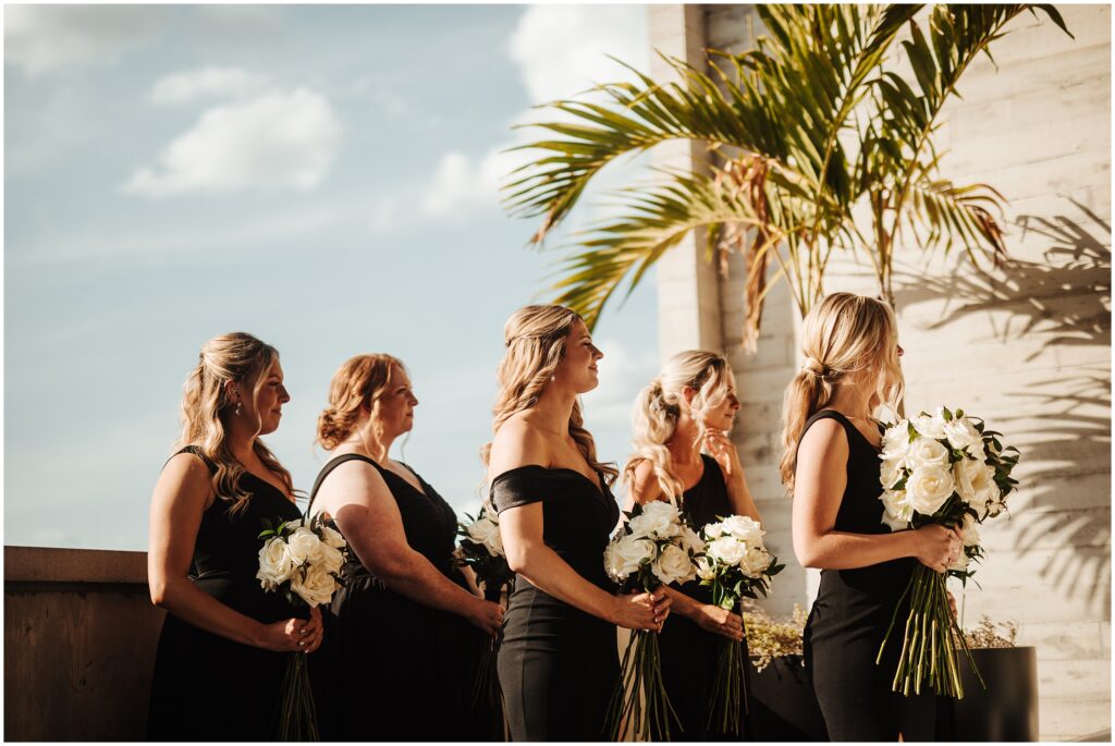 Bridesmaids in black dresses and hold white rose bouquets at tropical Florida wedding 