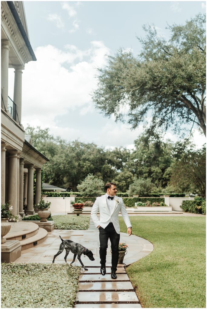 Portrait of groom in white jacket walking in a garden with dog before wedding