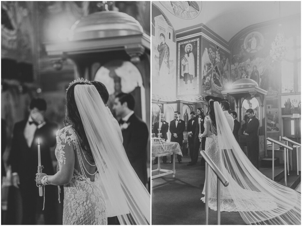 Bride with extra long wedding veil and train holds candle at altar of Greek Orthodox church during wedding ceremony