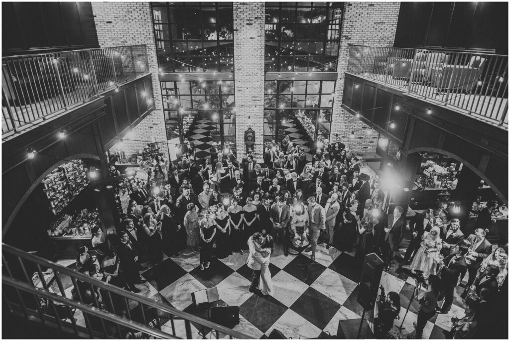 Black and white photo of bride and groom sharing first dance surrounded by guests at Oxford Exchange wedding 