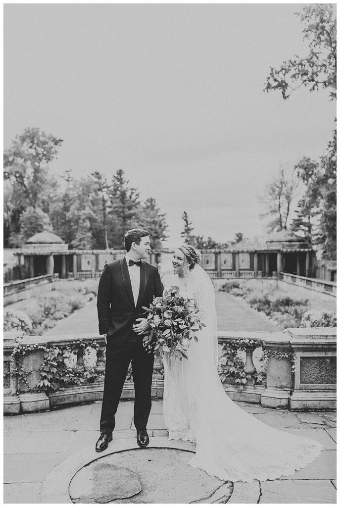 Black and white romantic portrait of groom standing next to bride who holds modern oversized bouquet 