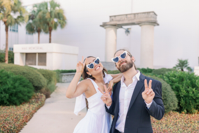 Playful bride and groom wearing heart sunglasses outside Tampa courthouse after their elopement