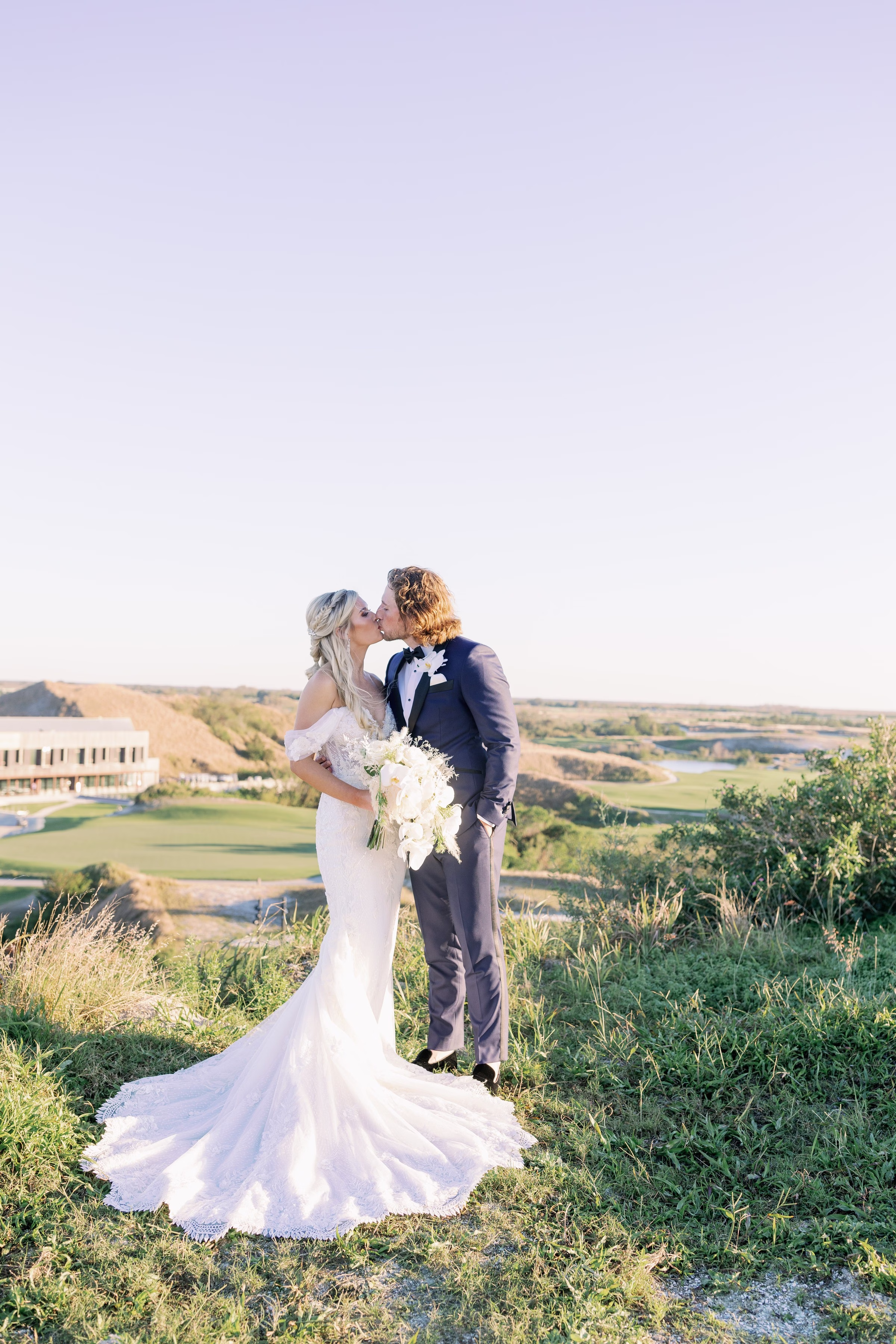 Bride and groom sharing romantic kiss in elegant wedding attire with white bouquet overlooking scenic Tampa Bay landscape captured by Ashley Izquierdo Photography
