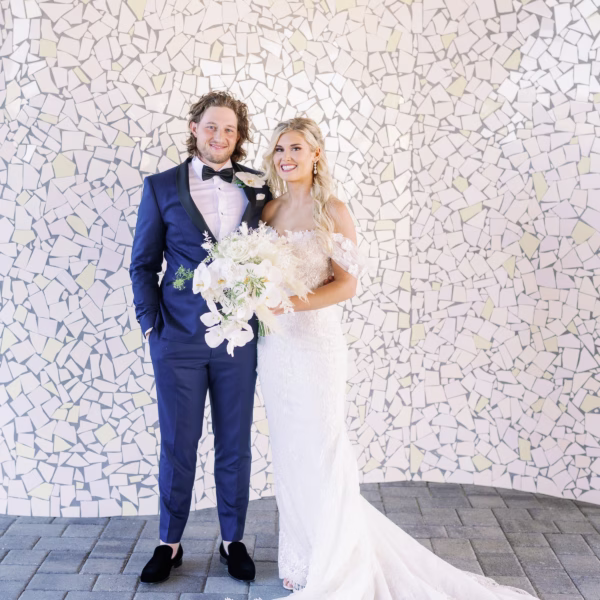 Bride and groom pose together against white mosaic tile wall during Tampa Bay wedding photographed by Ashley Izquierdo Photography