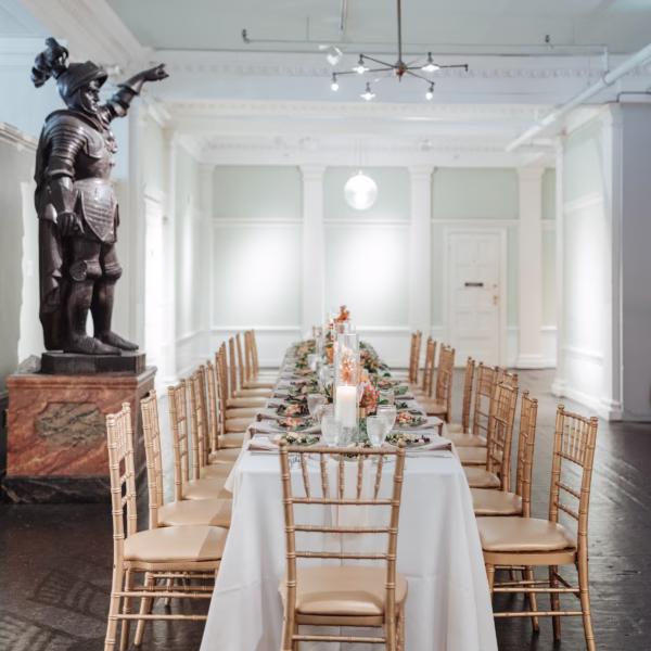 Elegant white wedding reception table with gold chiavari chairs and floral centerpieces in historic venue with classical architecture statue