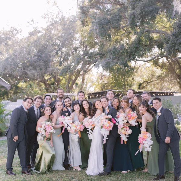 Large wedding party group photo with bridesmaids in sage green dresses and groomsmen in dark suits holding colorful bouquets at outdoor Tampa Bay wedding venue