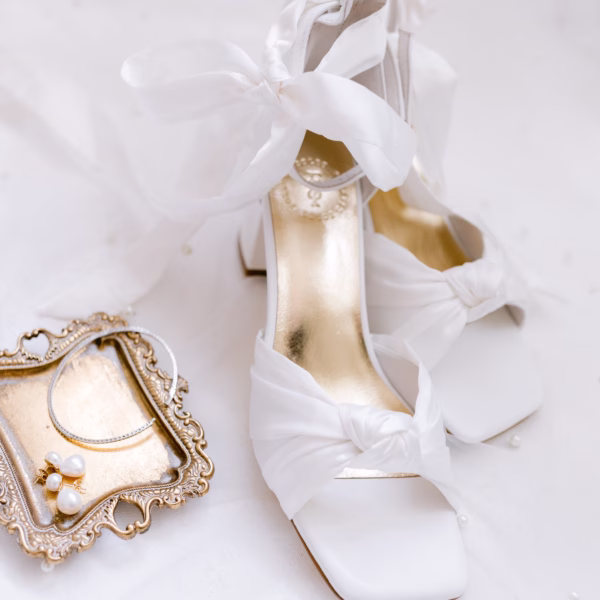White wedding shoes with ribbon ties displayed alongside pearl jewelry on ornate vintage tray captured by Tampa Bay wedding photographer Ashley Izquierdo Photography