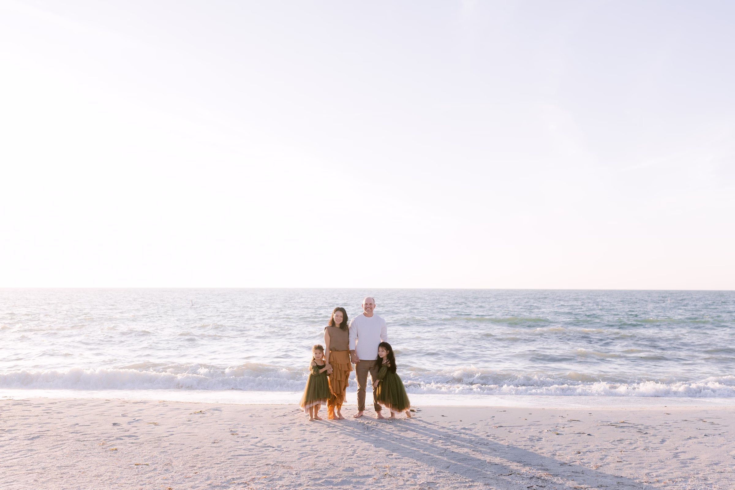 Tampa Bay beach family photography session by Ashley Izquierdo Photography featuring family of four in coordinated earth tones on sandy shoreline