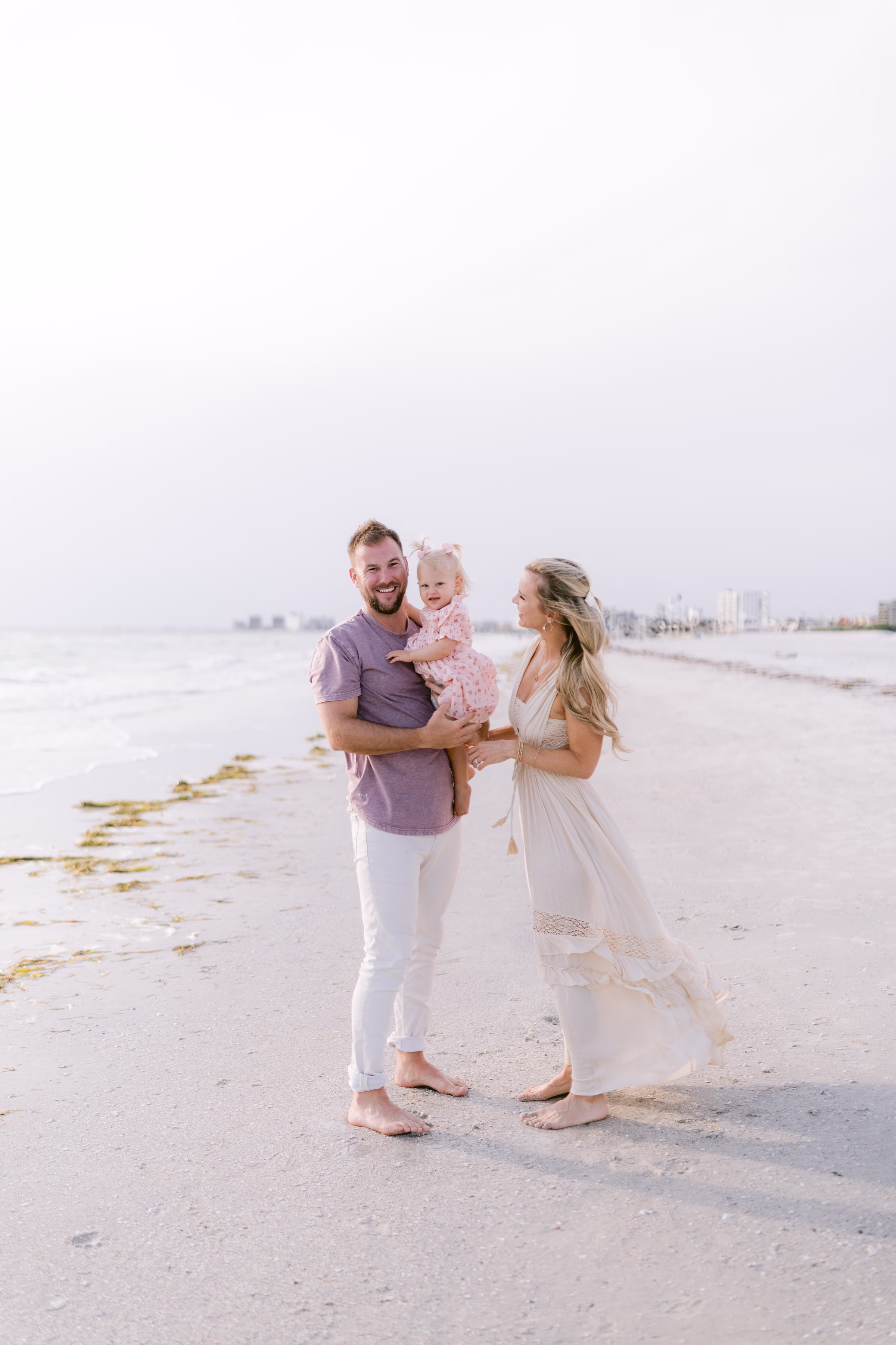 Tampa Bay family beach photography session by Ashley Izquierdo Photography featuring parents with toddler on sandy shoreline