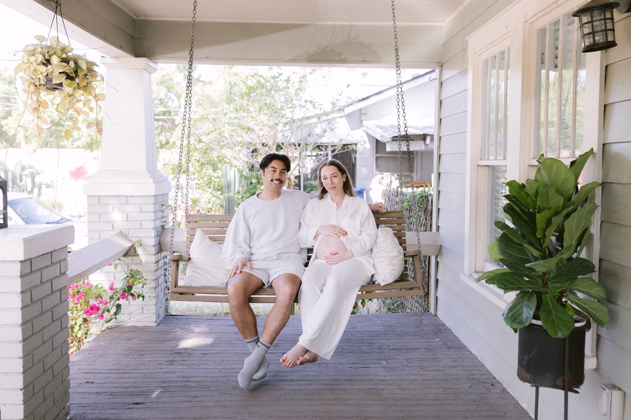 Expecting couple in white robes sitting on front porch swing during maternity session photographed by Ashley Izquierdo Photography in Tampa Bay