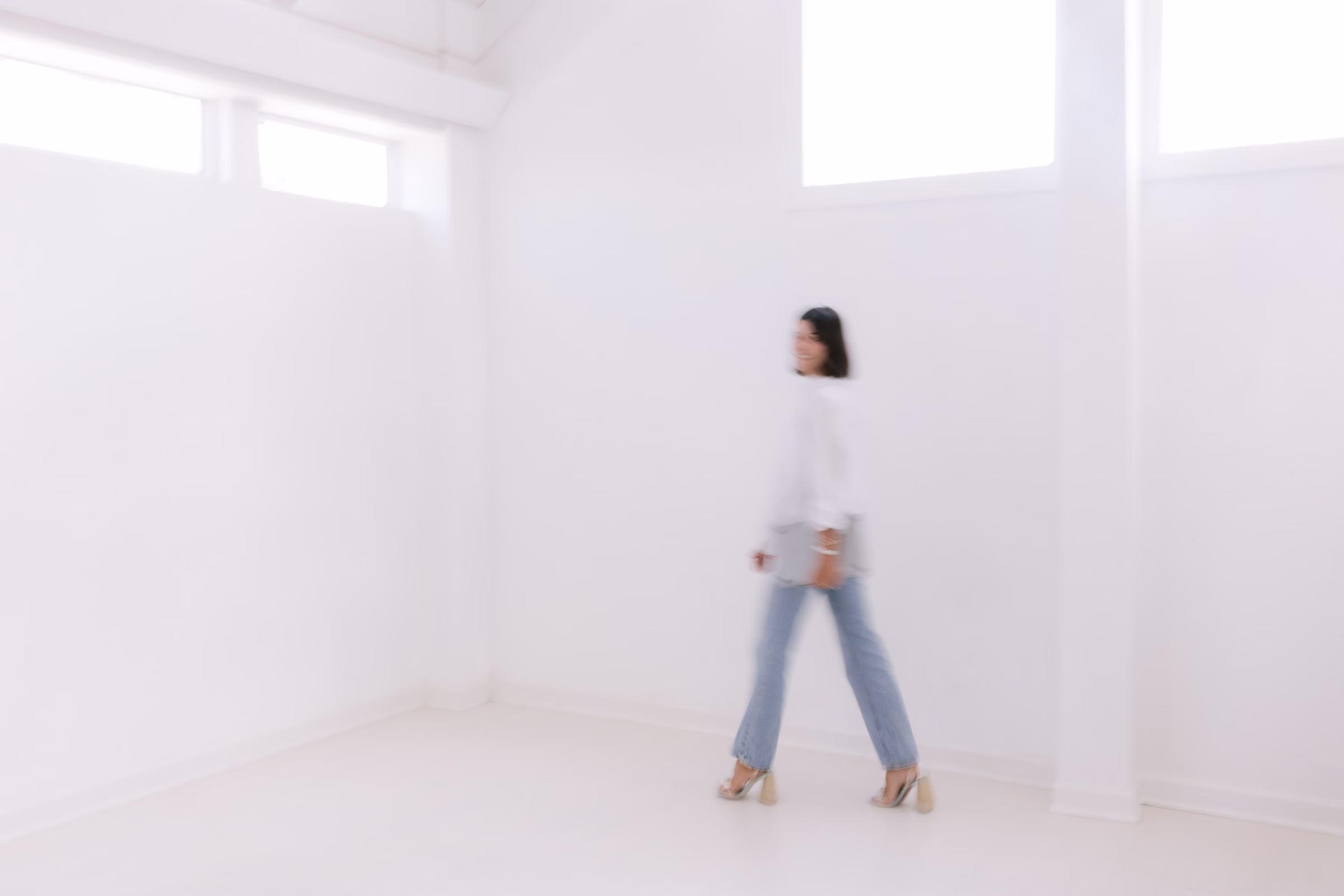 Woman in motion blur white top and jeans walking through bright minimalist white studio space captured by Tampa Bay wedding photographer Ashley Izquierdo Photography