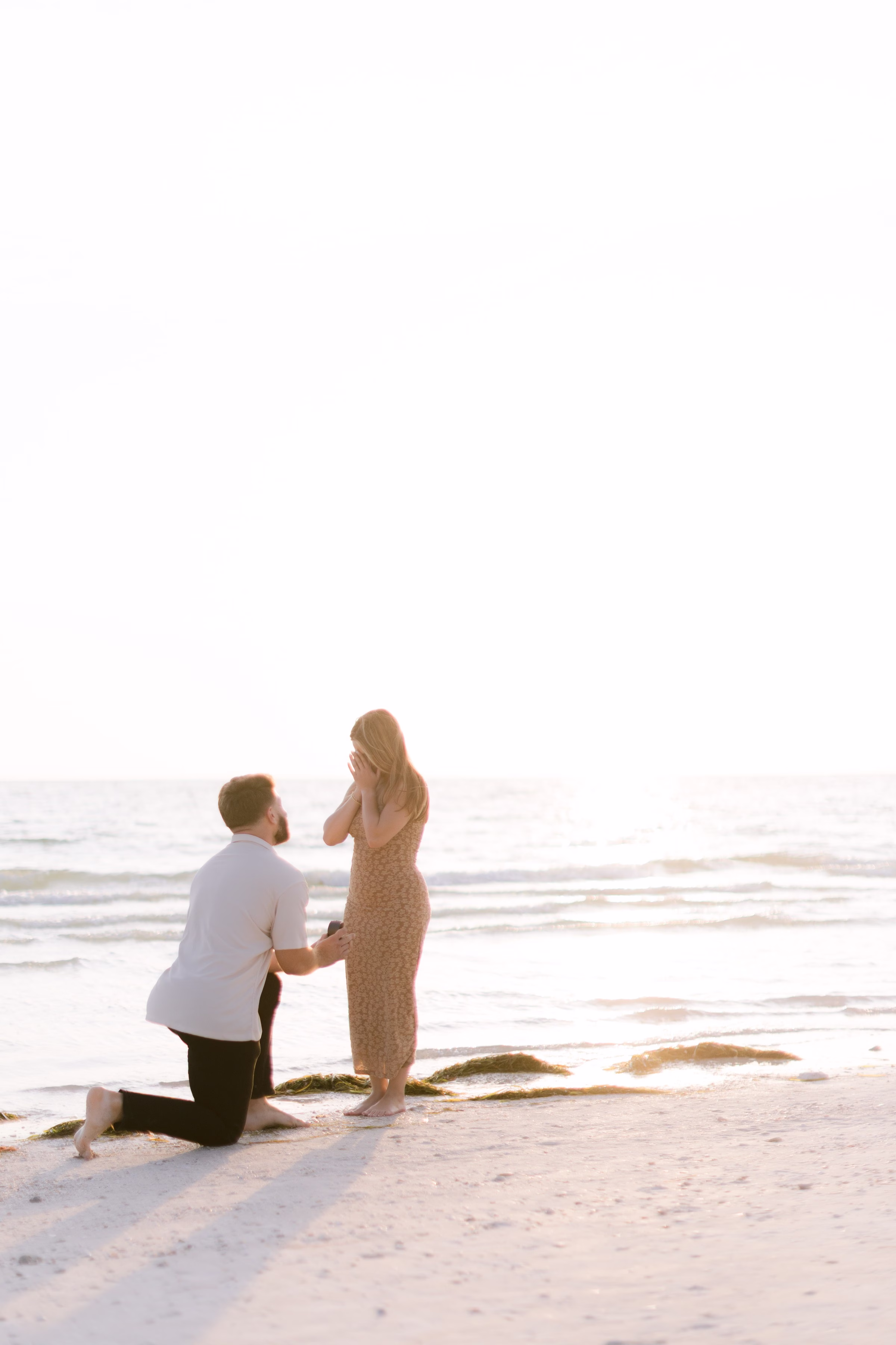 Romantic beach proposal at sunset captured by Tampa Bay wedding photographer Ashley Izquierdo Photography showing couple on sandy shore with ocean waves