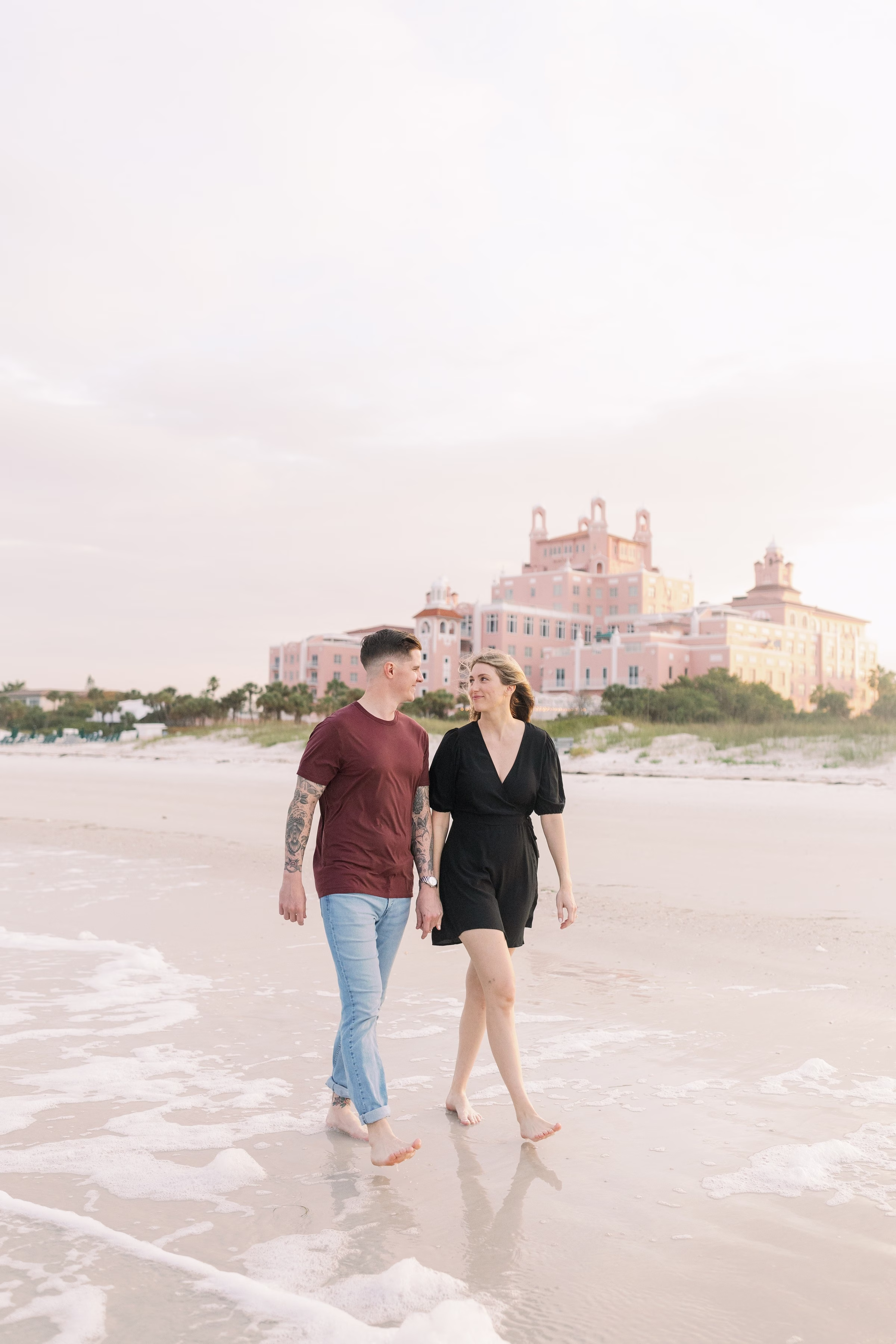 Engaged couple walking on St. Pete Beach with the iconic pink Don CeSar Hotel in the background during their Tampa Bay engagement session