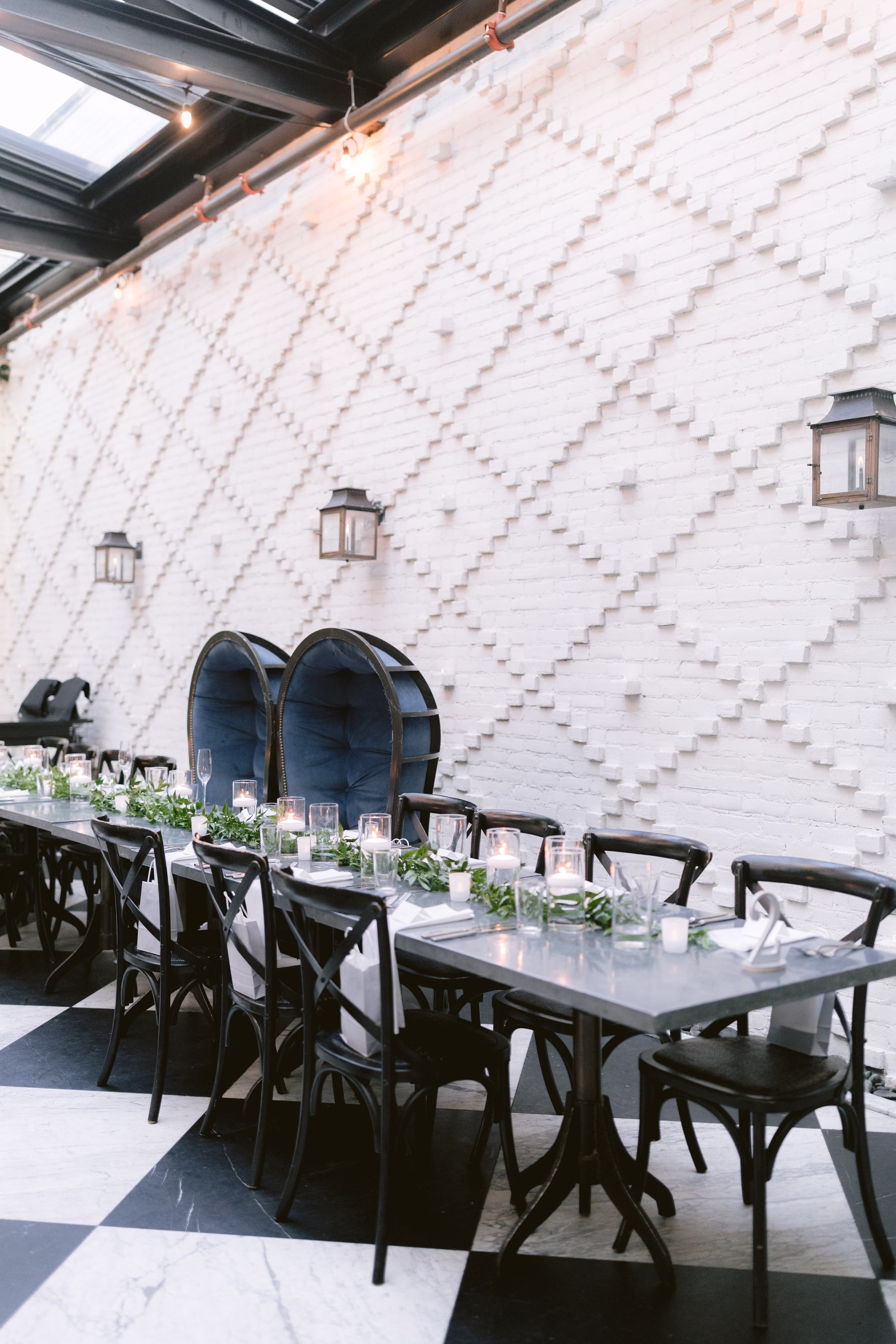 Elegant reception dinner tables with black chairs and candle centerpieces against textured white brick wall at Tampa Bay wedding venue