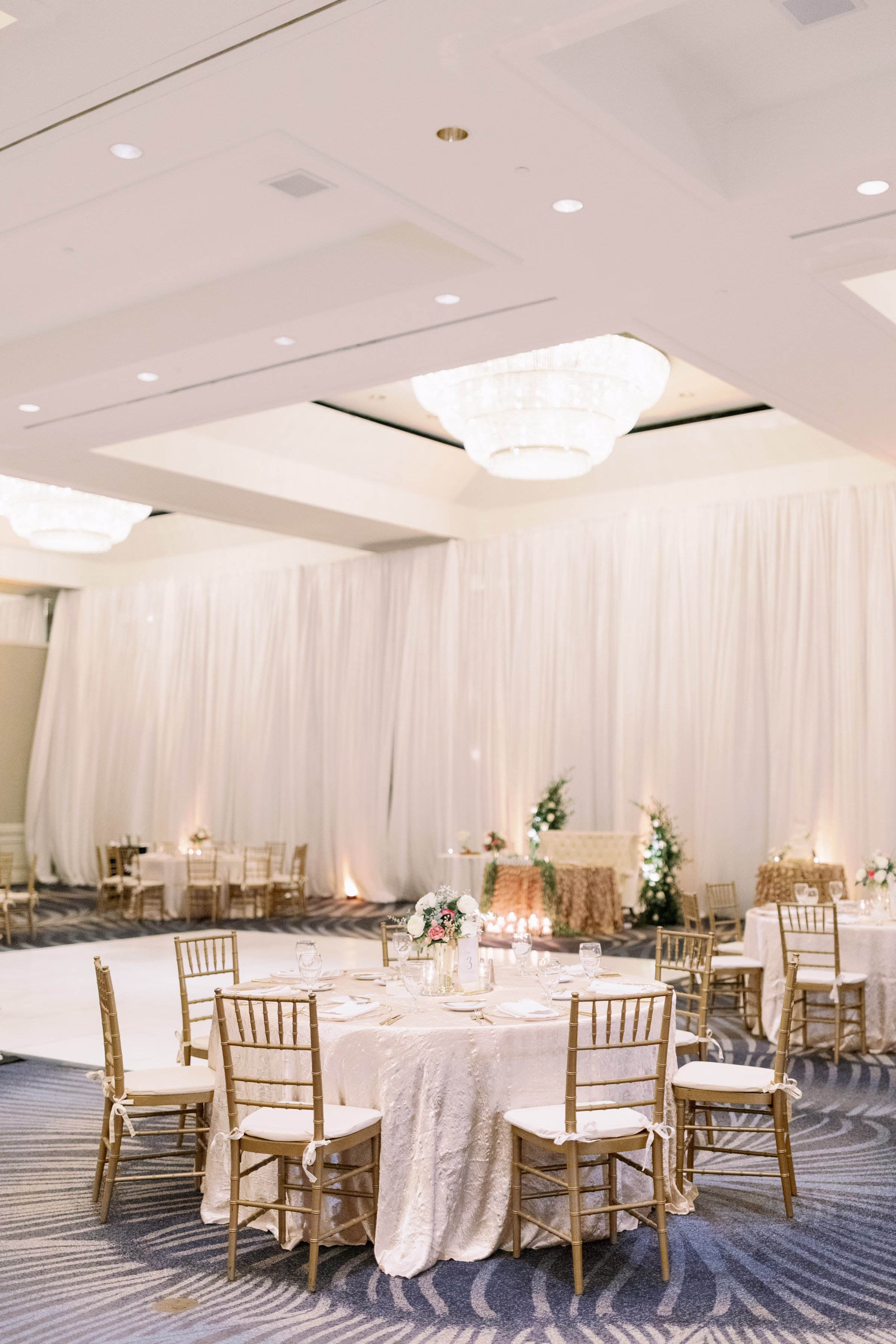 Elegant white and gold wedding reception with round tables, gold chiavari chairs, and white linens at Tampa Bay venue photographed by Ashley Izquierdo Photography