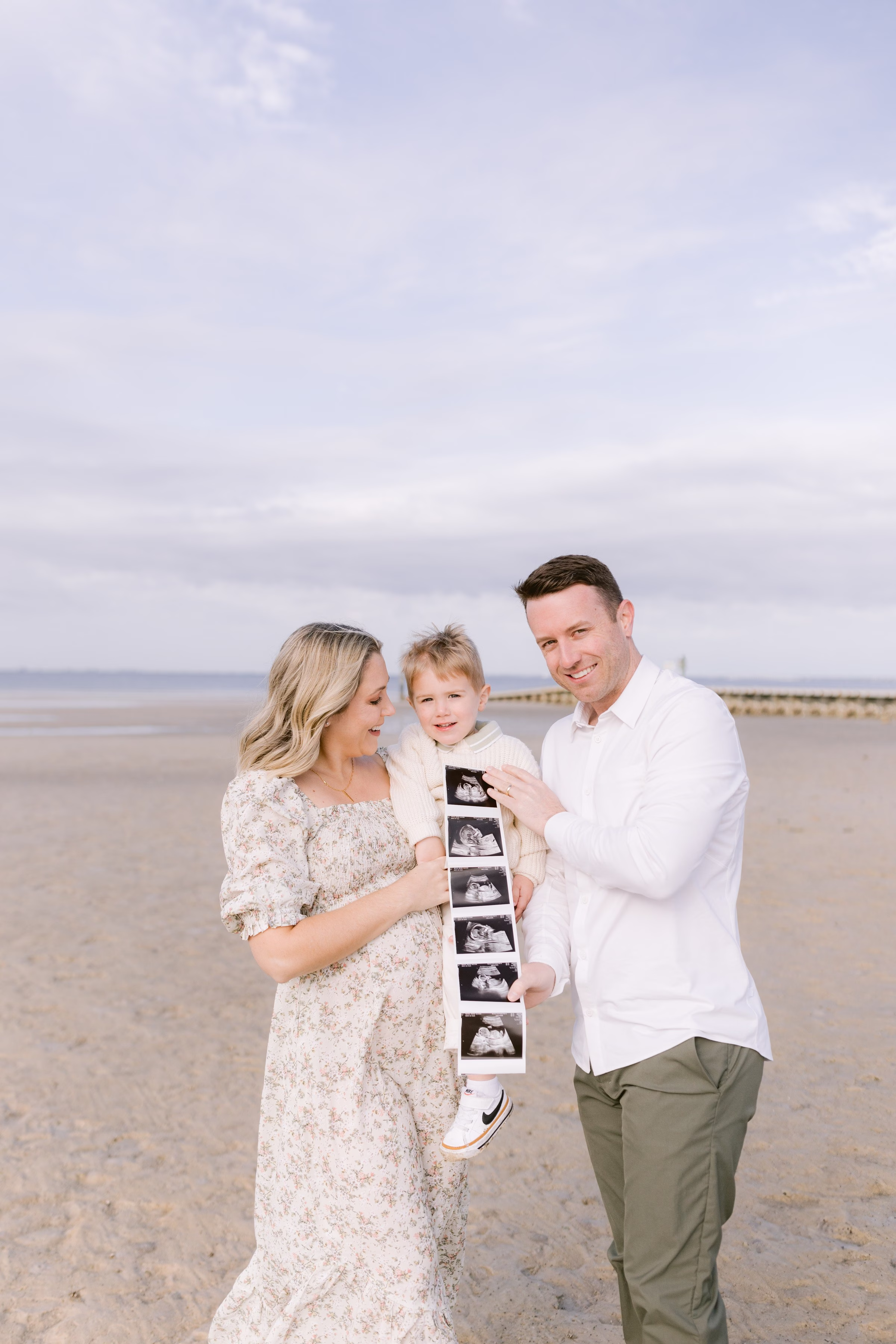 Family maternity announcement photo with ultrasound photos on Tampa Bay beach by Ashley Izquierdo Photography