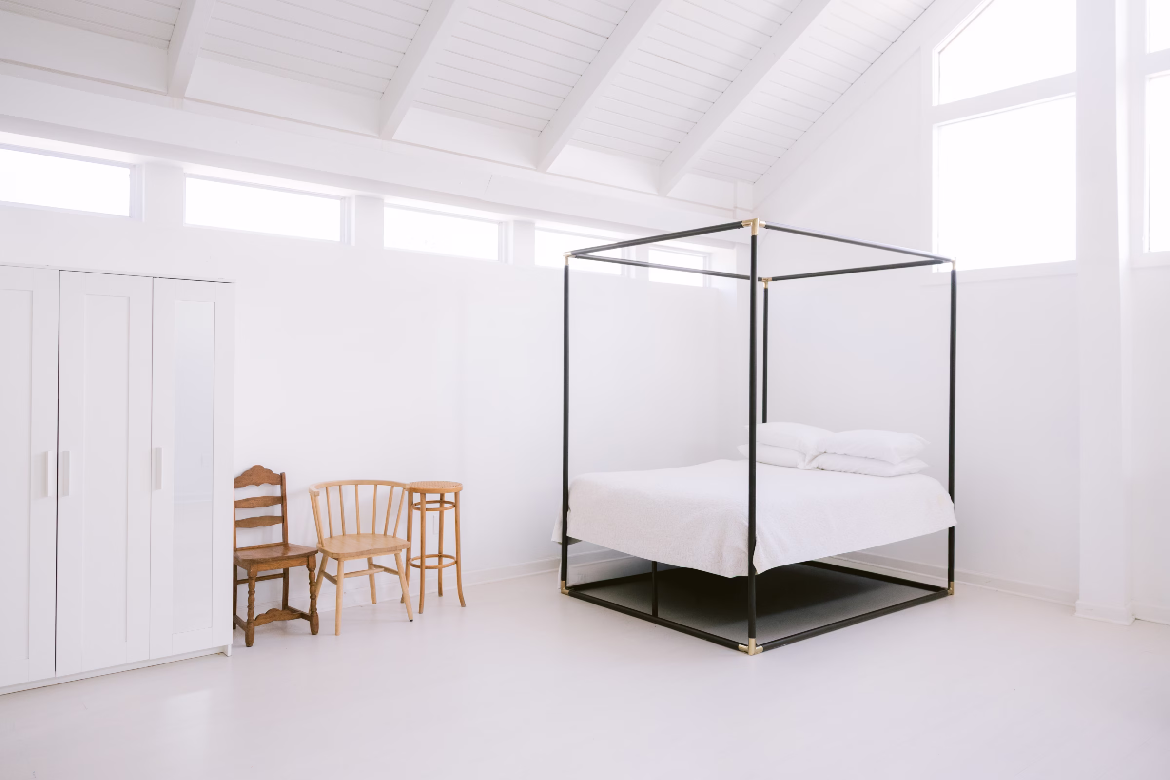 Minimalist white bedroom with black four-poster bed and exposed beam ceiling at Tampa Bay photo studio