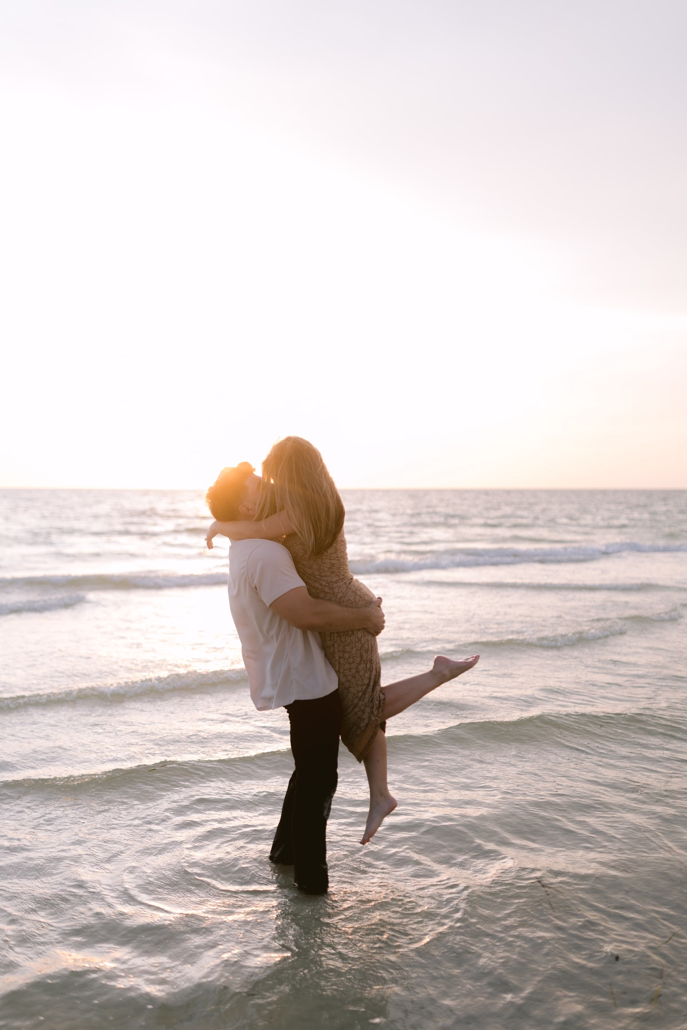 Romantic beach engagement session at sunset in Tampa Bay with couple embracing in ocean waves photographed by Ashley Izquierdo Photography