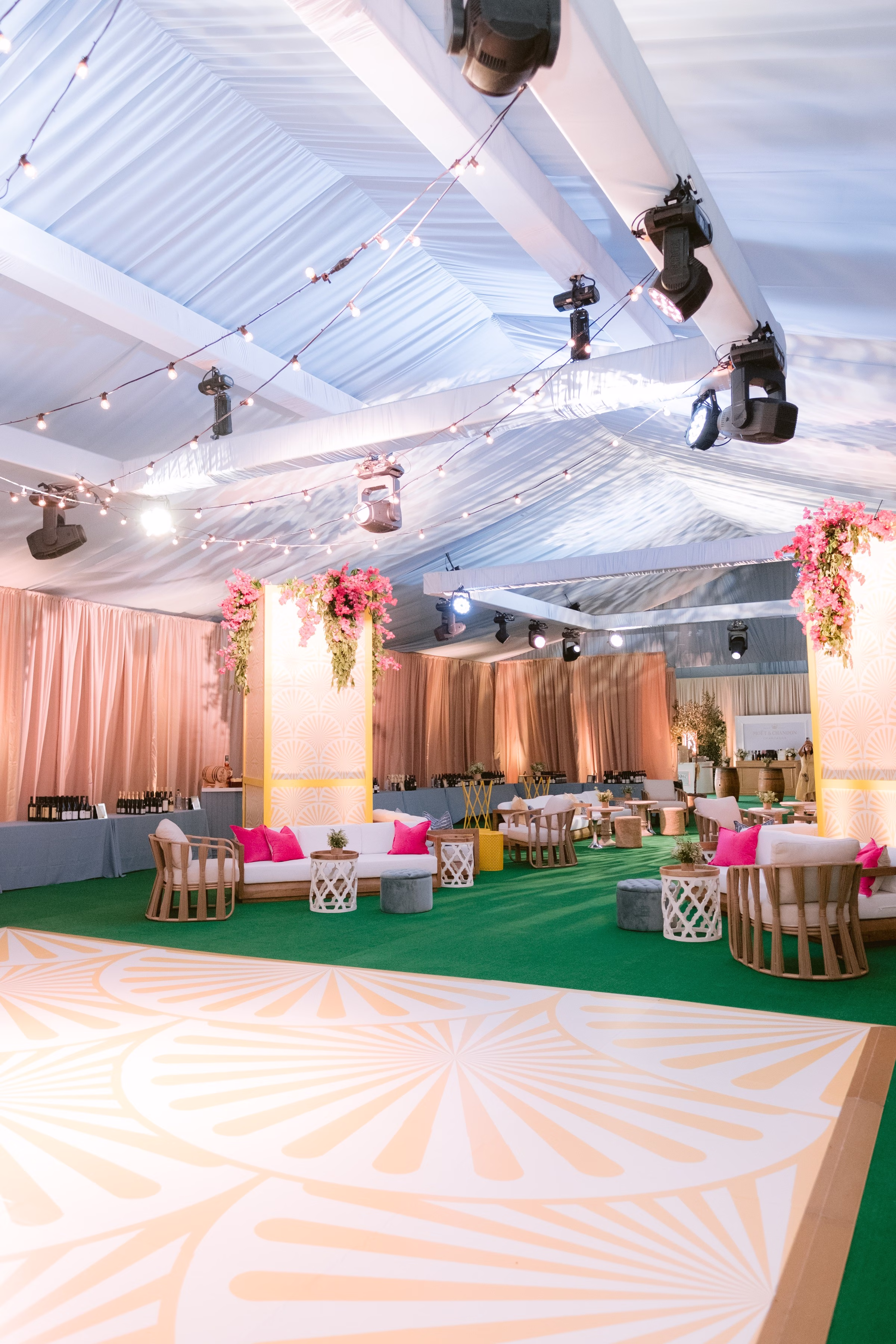 Elegant corporate event space with white tent ceiling, string lights, pink floral arrangements, green carpet, and modern lounge seating photographed by Tampa Bay photographer Ashley Izquierdo Photography