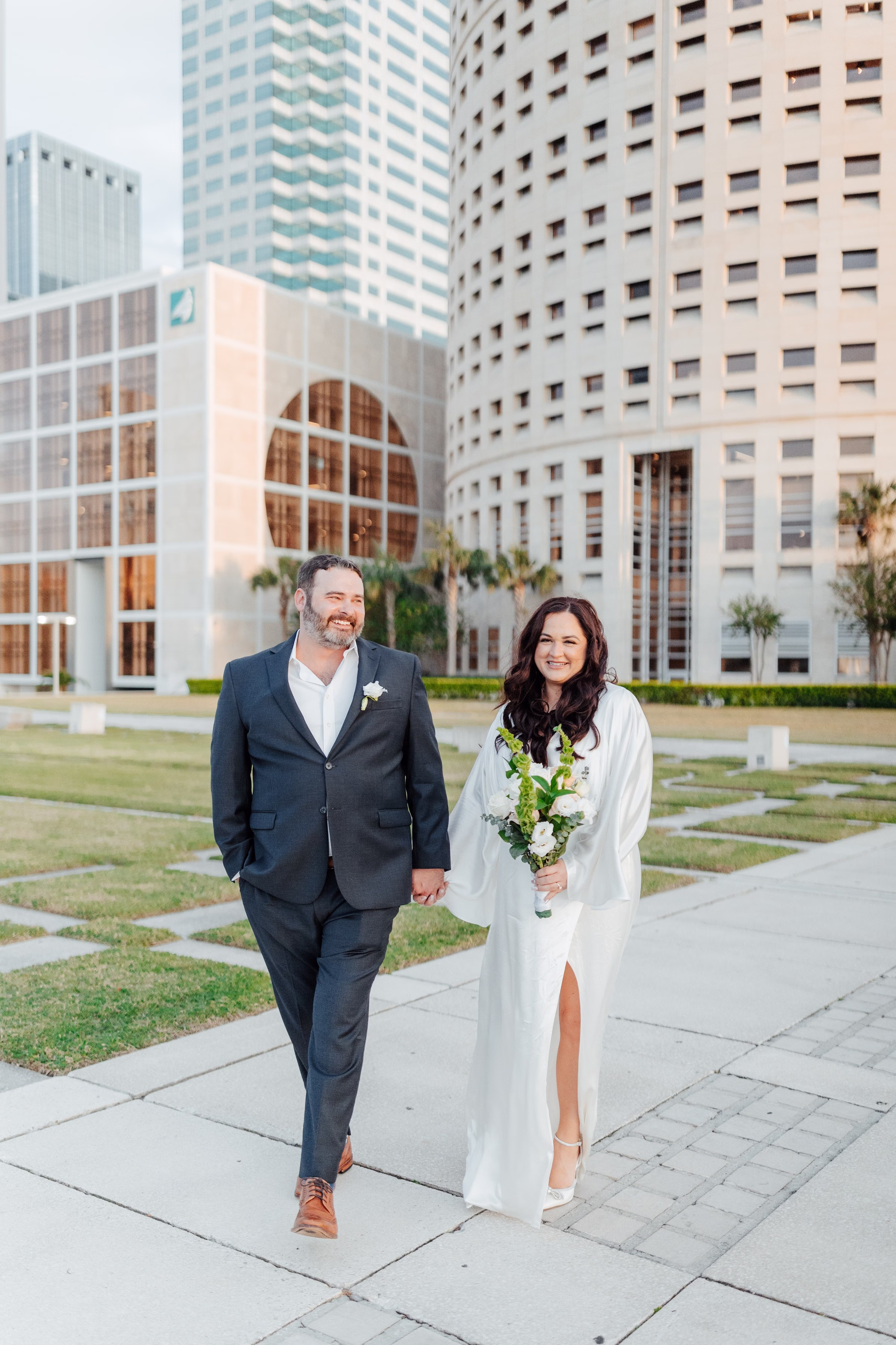 Newlywed couple walking hand in hand through downtown Tampa urban setting after intimate elopement ceremony captured by Ashley Izquierdo Photography