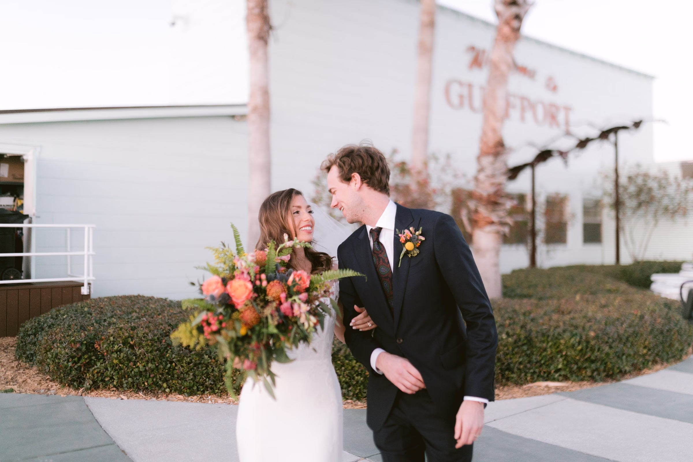 Bride and groom walking together after their Tampa Bay wedding ceremony, bride carrying colorful bouquet with coral and yellow flowers