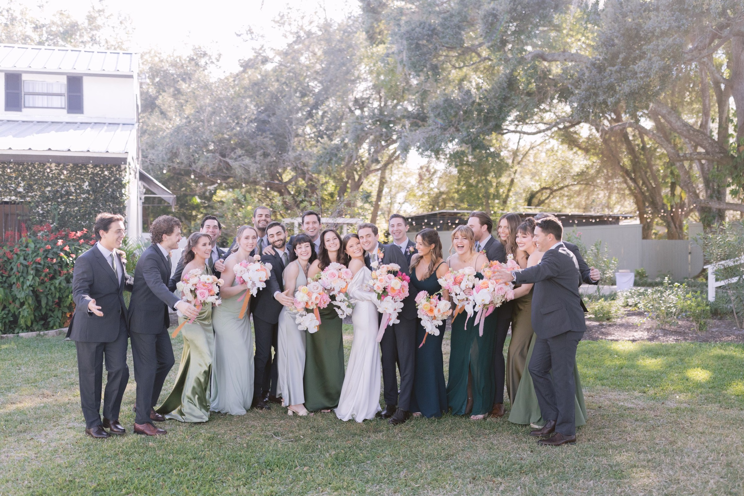tampa bay wedding party sb gardens venue group photo - Experience Large wedding party group photo with bridesmaids in green dresses and groomsmen in black suits holding pink bouquets at SB Gardens Tampa Bay wedding venue