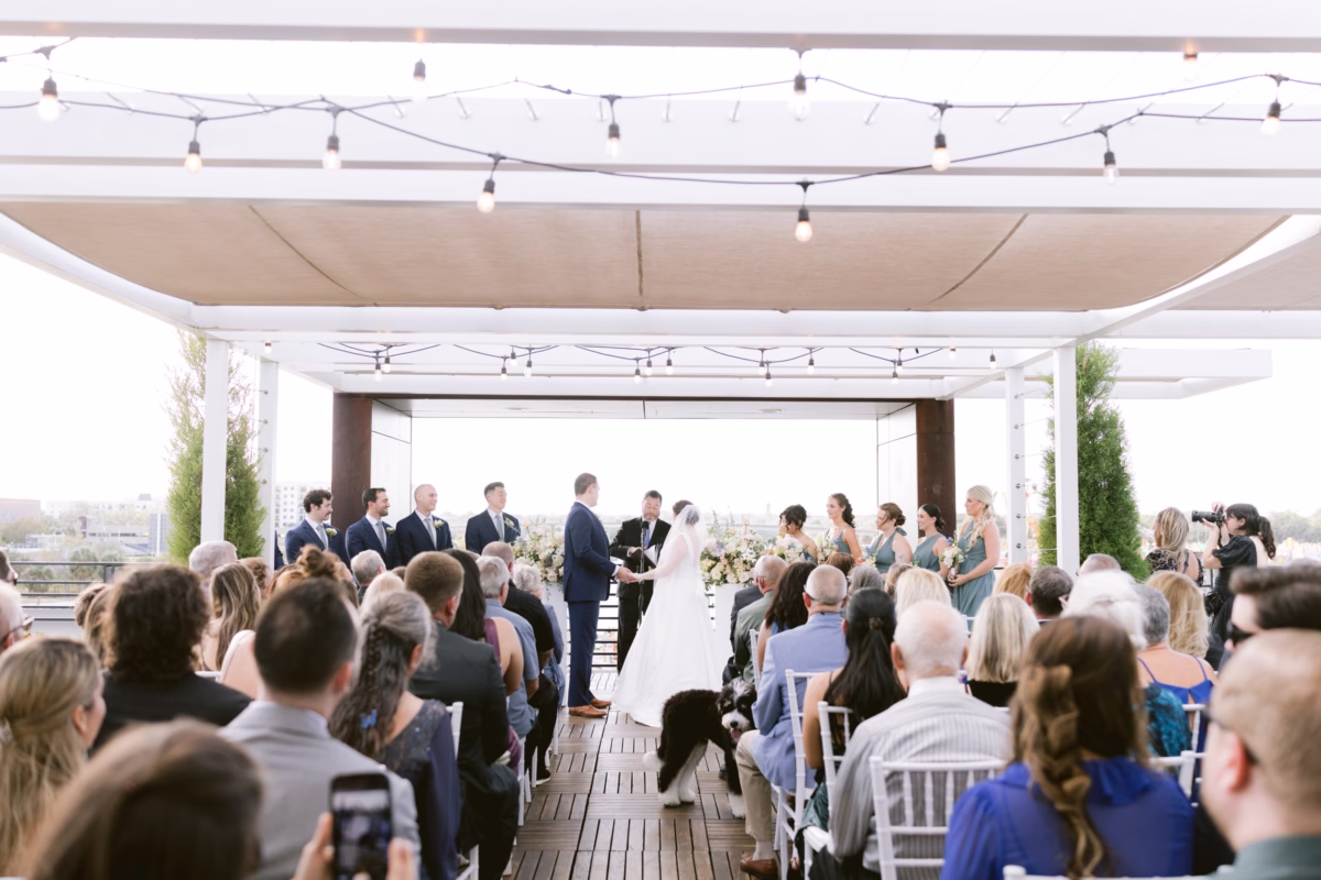 Rooftop wedding ceremony at Armature Works in Tampa with string lights overhead, planned by Logan Paradiso and florals by I Dew Events