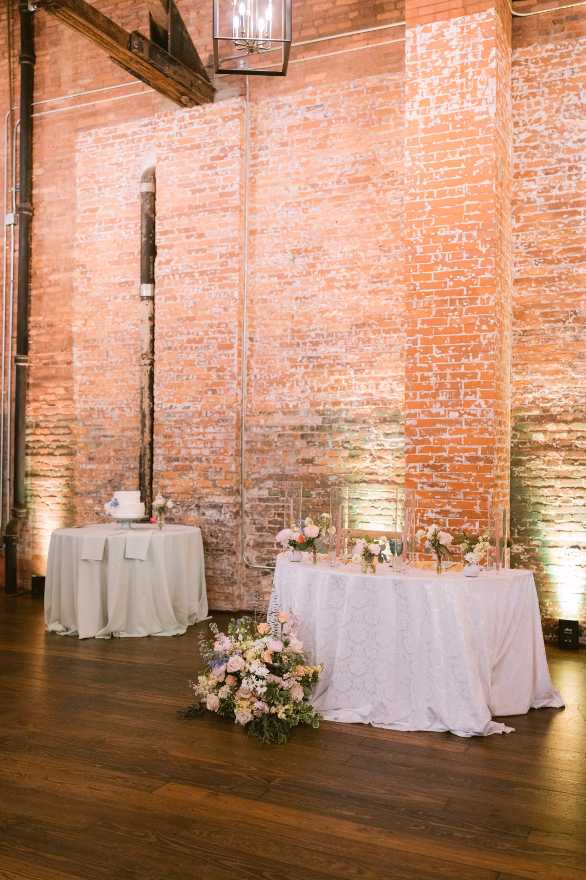 Elegant sweetheart table with pink floral arrangements by I Dew Events at Armature Works Tampa wedding reception featuring exposed brick walls and romantic lighting