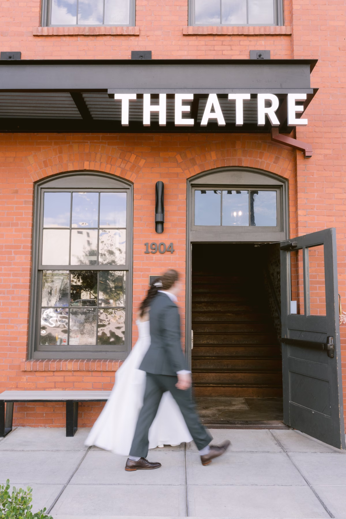 Bride and groom walking past the historic 1904 theatre entrance at Armature Works wedding venue in Tampa captured by Ashley Izquierdo Photography