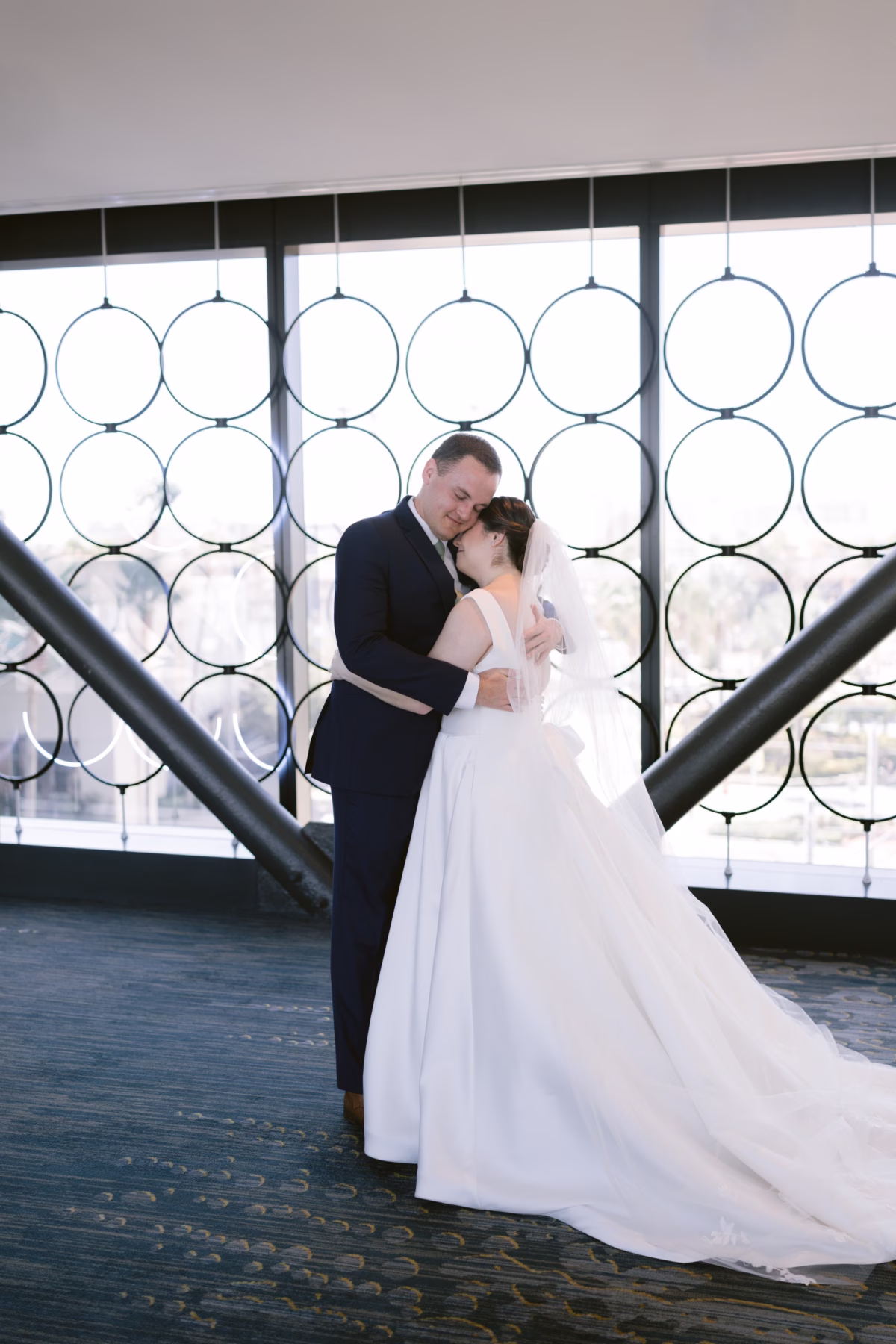 Bride and groom embrace in elegant portrait at Armature Works Tampa wedding venue with modern circular window design, captured by Ashley Izquierdo Photography