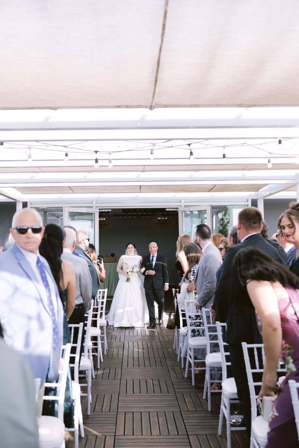 Bride walking down the aisle with father during outdoor wedding ceremony at Armature Works Tampa planned by Logan Paradiso