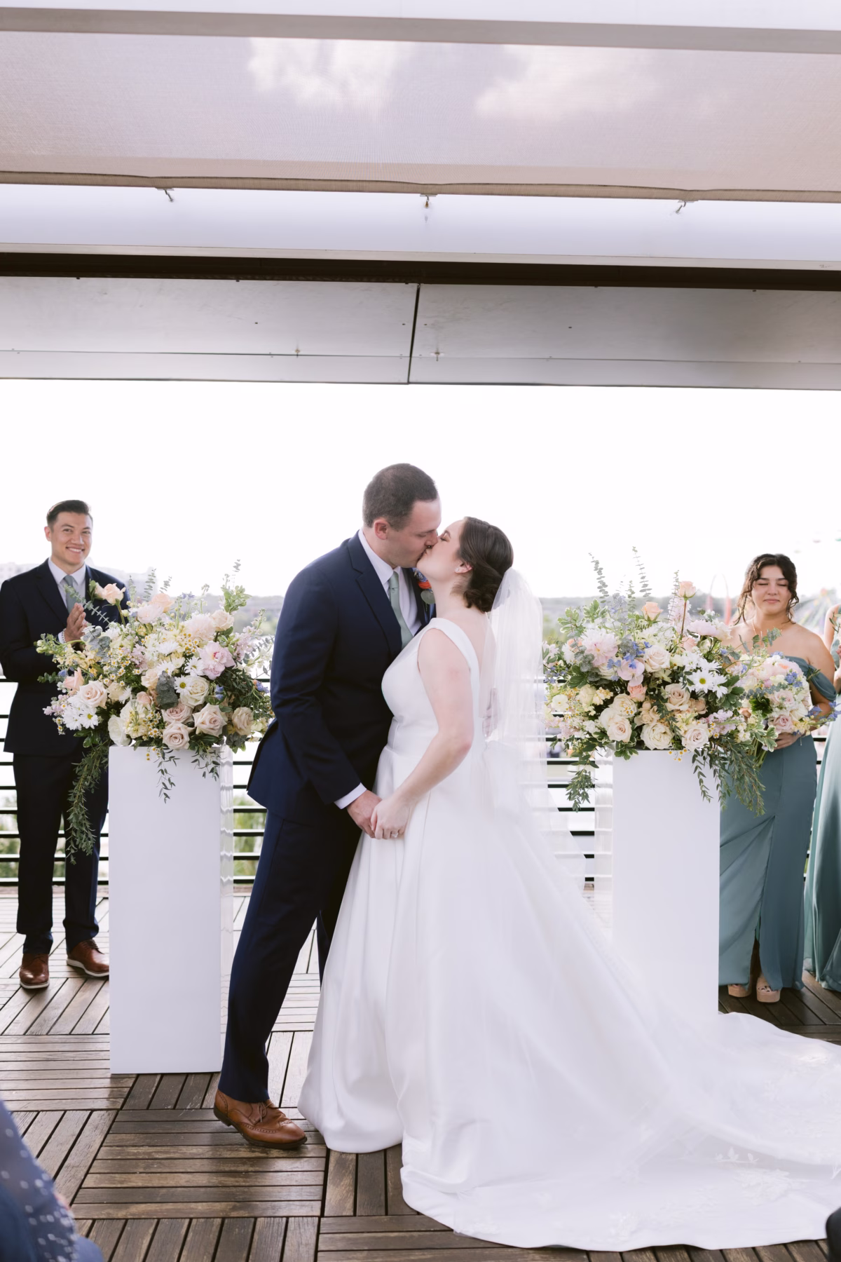 Bride and groom share first kiss during outdoor wedding ceremony with lush floral arrangements by I Dew Events at Armature Works in Tampa
