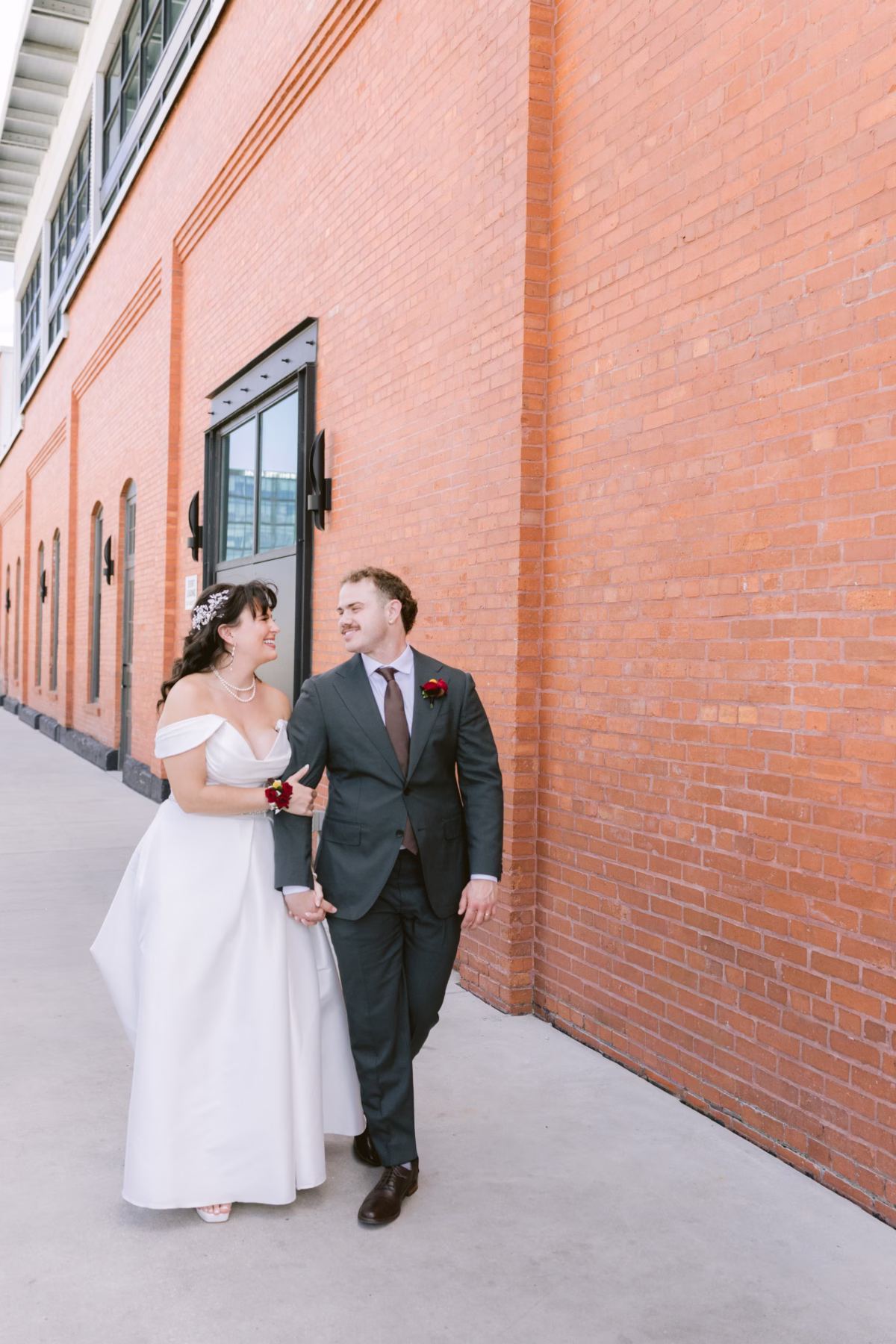 Bride and groom walking together at Armature Works venue with red brick wall backdrop in Tampa photographed by Ashley Izquierdo Photography