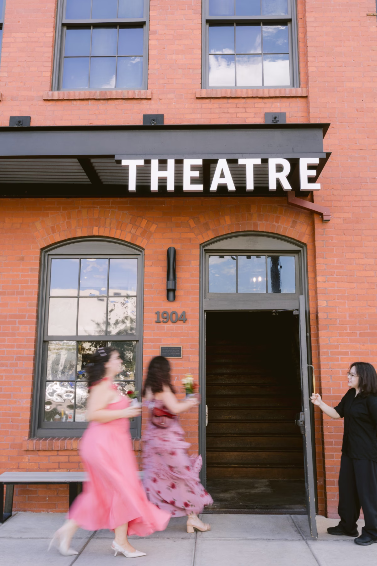 Wedding couple in pink gowns running past historic Armature Works theatre entrance during Tampa Bay wedding planned by Seashine Weddings